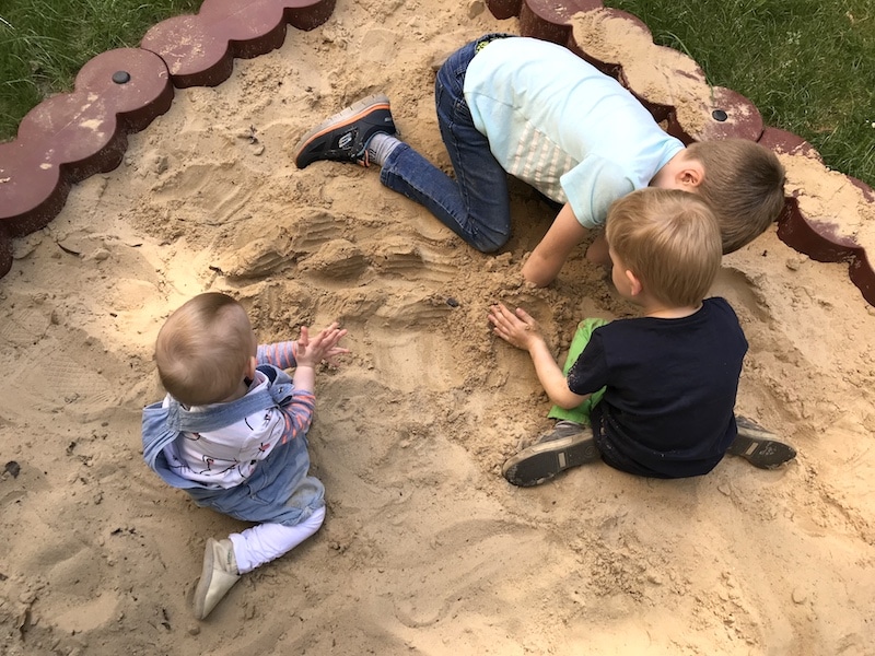 Drei Kinder spielen im Sandkasten.