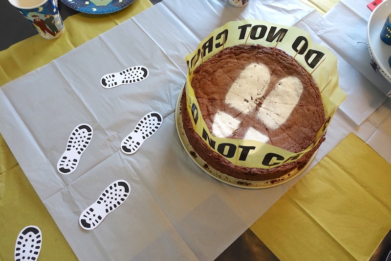 Einfacher Kuchen zur Detektiv-Party: mit Schablone Puderzucker auf den Schokokuchen sieben. Das Absperrband ist cool! | Mehr Infos zum Essen, Deko und Spielen auf dem Detektiv-Geburtstag auf Mamaskind.de